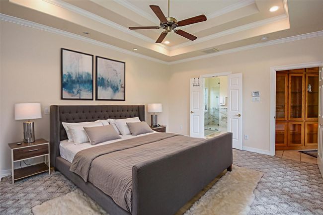 Spacious room featuring a patterned carpet, tray ceiling with recessed lighting, and a ceiling fan. It has double doors leading to a tiled bathroom with a glass shower. There's also built-in shelving on the side. *Virtually staged | Image 27