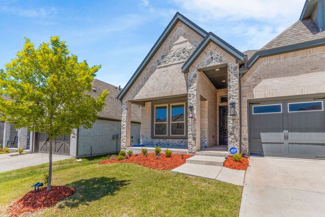 French country inspired facade featuring driveway, brick siding, an attached garage, and a front yard | Image 4