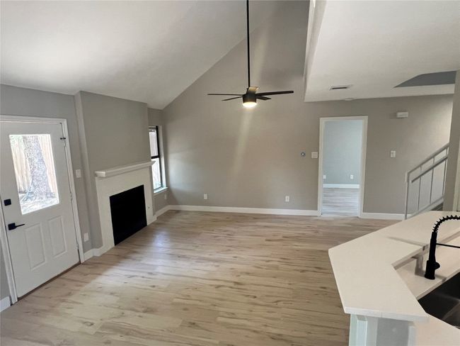 Unfurnished living room with light wood-style floors, a fireplace, stairs, a ceiling fan, and high vaulted ceiling | Image 9