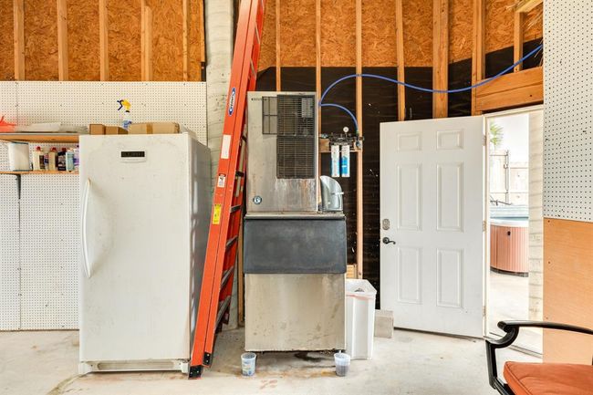 The ground floor includes an ice maker and additional freezer in the garage or workshop, featuring pegboard walls, . There's an open door leading outside, and some storage shelves with various items. The space is functional and organized. | Image 48