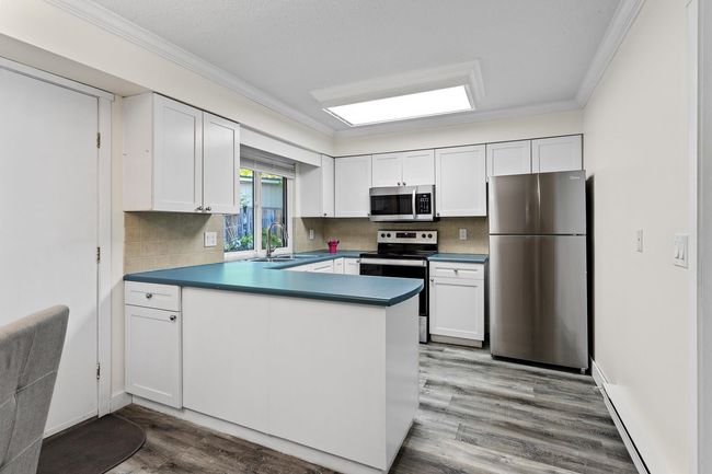 Kitchen featuring a sink, stainless steel appliances, crown molding, a peninsula, and wood finished floors | Image 6