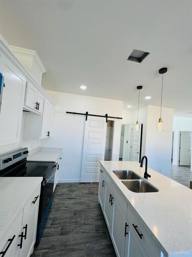 Kitchen with white cabinetry, sink, range with electric stovetop, and a barn door | Image 5