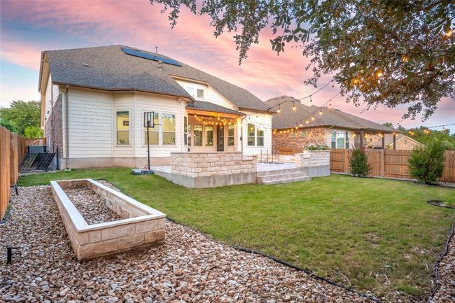 Rear view of house with a patio, a fenced backyard, roof with shingles, roof mounted solar panels, and a garden | Image 37