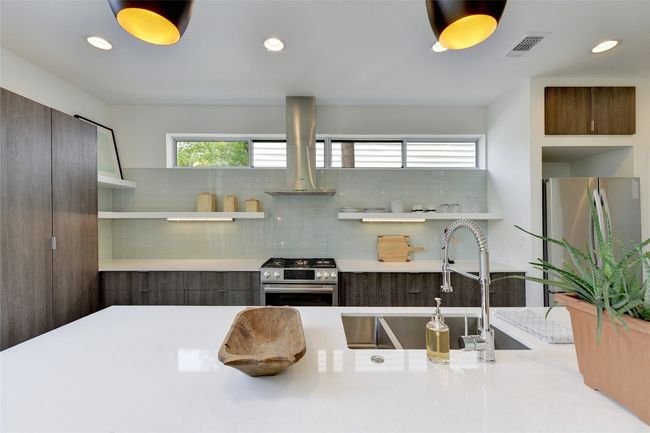 Kitchen with open shelves, a sink, island exhaust hood, decorative backsplash, and stainless steel appliances | Image 7