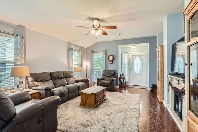 Living room with dark wood finished floors, vaulted ceiling, visible vents, baseboards, and ceiling fan | Image 7