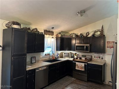 Kitchen featuring dark hardwood / wood-style floors, sink, hanging light fixtures, decorative backsplash, and stainless steel appliances | Image 2