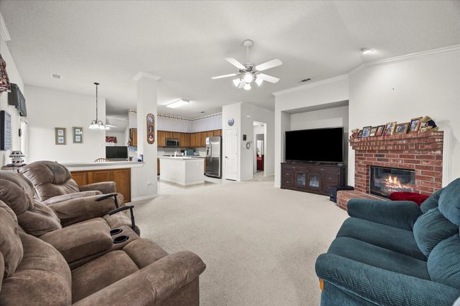 Living room featuring a ceiling fan, a fireplace, light colored carpet, and ornamental molding | Image 15