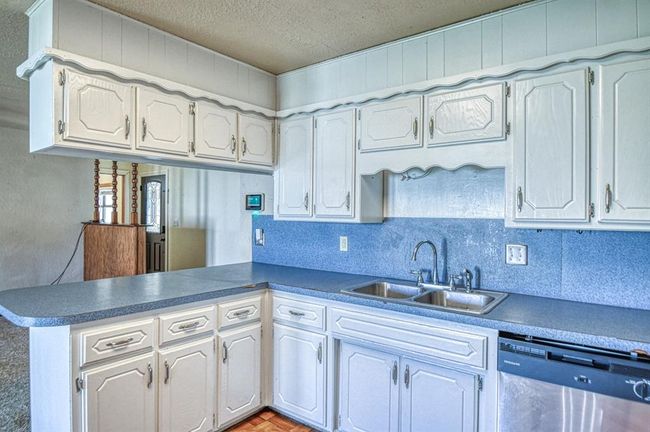 Kitchen featuring stainless steel dishwasher, a sink, a peninsula, a textured ceiling, and decorative backsplash | Image 9