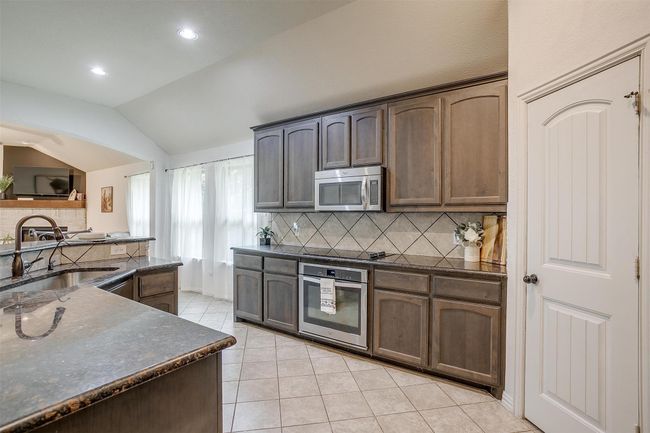 Kitchen featuring stainless steel appliances, light tile patterned floors, decorative backsplash, vaulted ceiling, and dark stone countertops | Image 15