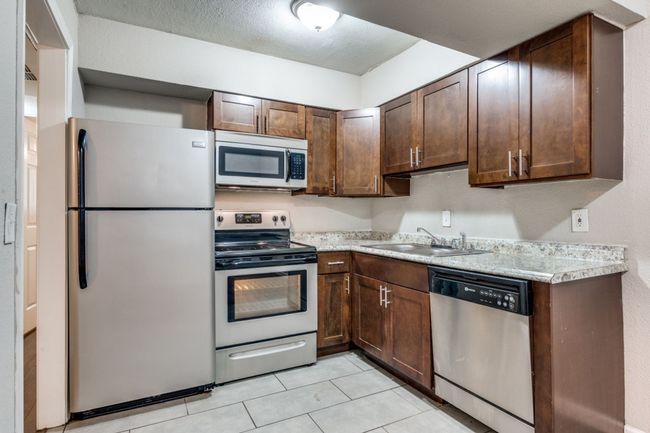 Kitchen featuring stainless steel appliances, light countertops, dark brown cabinetry, and light tile patterned floors | Image 6