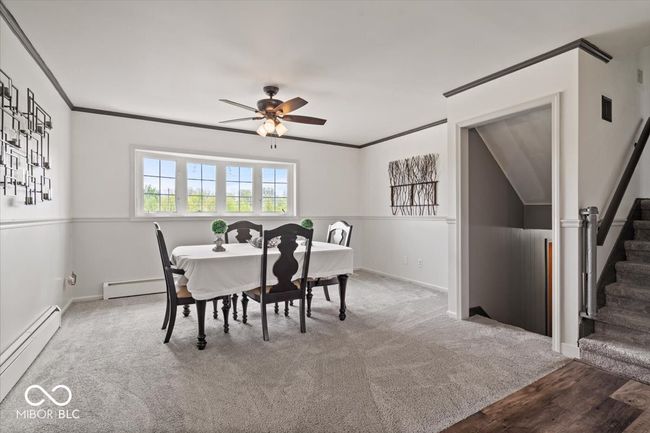 carpeted dining room featuring a baseboard heating unit, stairs, a ceiling fan, baseboards, and ornamental molding | Image 20