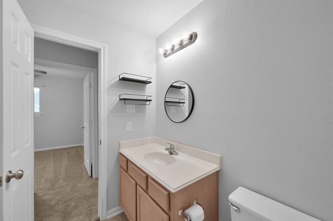 The upstairs bathroom features a light wood vanity with a crisp white countertop, complemented by a matching mirror. Wall-mounted black wire shelves add a contemporary touch and practical storage, while the clean lines and neutral finishes create a fresh, relaxing atmosphere. | Image 30