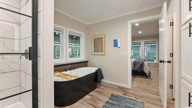Ensuite bathroom with a freestanding tub, baseboards, a marble finish shower, wood finished floors, and ornamental molding | Image 28