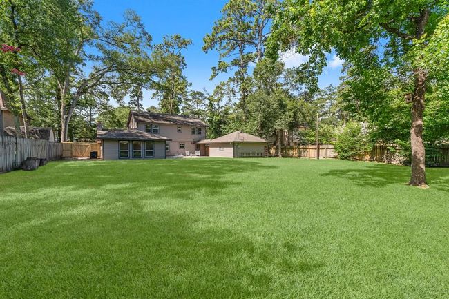 This photo shows a spacious backyard with a well-maintained lawn, surrounded by mature trees and a wooden fence for privacy. | Image 35