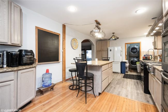 Kitchen featuring light wood-style flooring, a breakfast bar, arched walkways, stacked washing maching and dryer, and freestanding refrigerator | Image 11