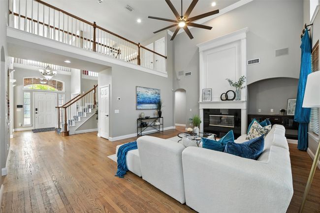 Living room with a towering ceiling, wood finished floors, a glass covered fireplace, ornamental molding, and stairs | Image 5