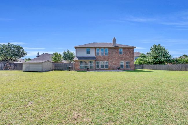 Back of house with brick siding, a fenced backyard, a storage shed, a chimney, and a patio area | Image 35