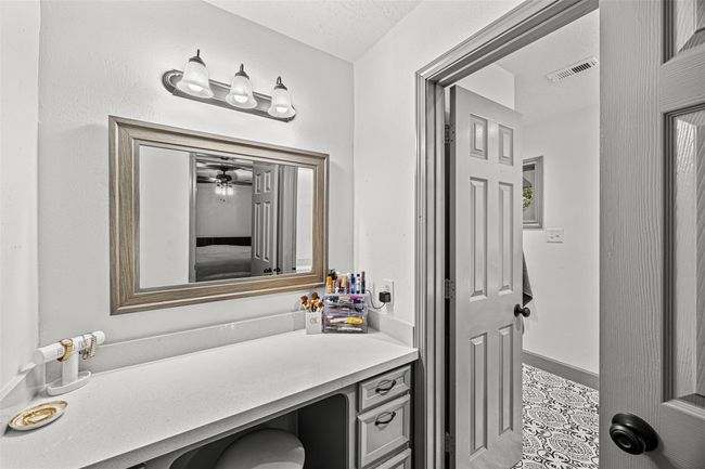 This photo showcases a modern bathroom with a sleek vanity area. It features a large mirror with a stylish frame and a three-light fixture above. The countertop is spacious, and the room is well-lit and airy. There's a view into an adjoining bathroom with decorative floor tiles. | Image 22