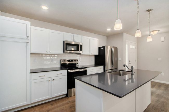 Bright, white kitchen cabinetry is accented by white quartz counters and tile backsplash. The kitchen island provides prep and sitting space and is accented by pendant lighting above. Stainless steel appliances are included! | Image 5