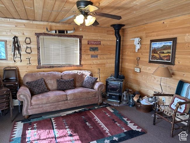 Carpeted living room featuring wood walls, a wood stove, a ceiling fan, and wooden ceiling | Image 15