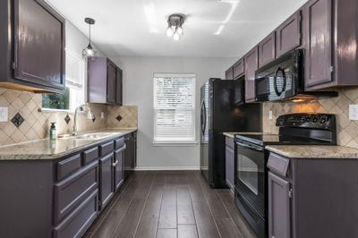 Kitchen with decorative light fixtures, tasteful backsplash, black appliances, dark wood-type flooring, and sink | Image 3