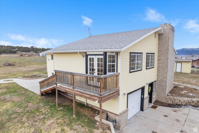 Rear view of house featuring french doors, concrete driveway, an attached garage, a shingled roof, and a chimney | Image 30
