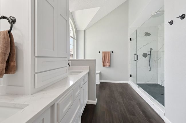 Bathroom featuring a marble finish shower, double vanity, wood finished floors, baseboards, and lofted ceiling | Image 22