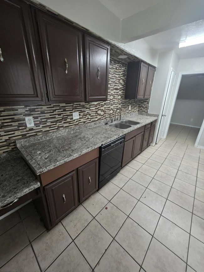 Kitchen with black dishwasher, light tile patterned floors, backsplash, and dark brown cabinets | Image 10