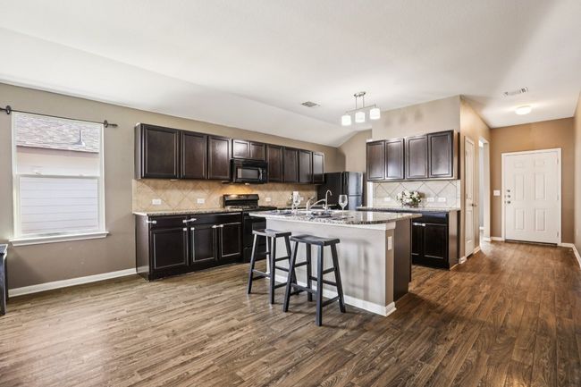 Kitchen featuring black appliances, a breakfast bar, backsplash, dark wood-style flooring, and dark brown cabinetry | Image 11