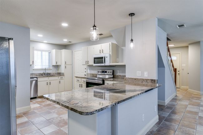 Kitchen with appliances with stainless steel finishes, a peninsula, stone counters, white cabinets, and hanging light fixtures | Image 10