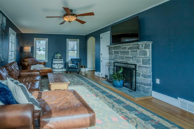 Living room featuring ceiling fan, a baseboard radiator, crown molding, wood-type flooring, and a fireplace | Image 4