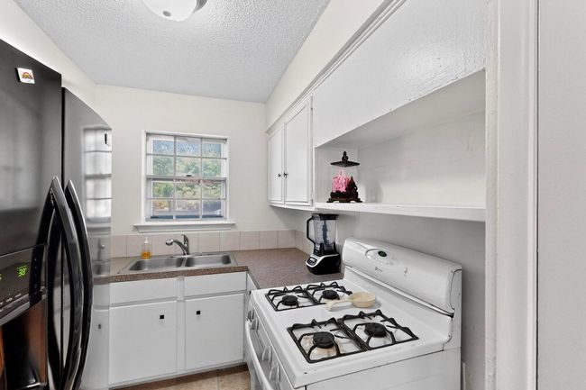 Kitchen with gas range gas stove, freestanding refrigerator, white cabinetry, a textured ceiling, and open shelves | Image 7