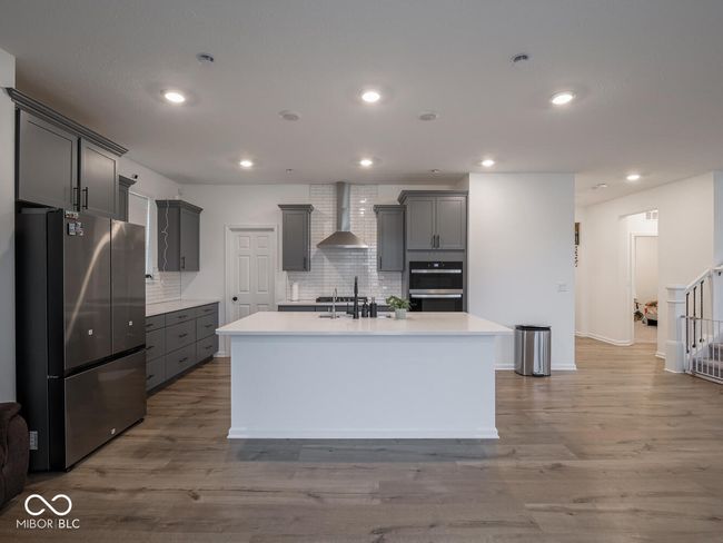 kitchen with wall chimney exhaust hood, gray cabinets, wood finished floors, a sink, and stainless steel appliances | Image 17
