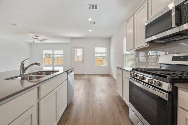 Kitchen with stainless steel appliances, light wood finished floors, decorative backsplash, ceiling fan, and recessed lighting | Image 14