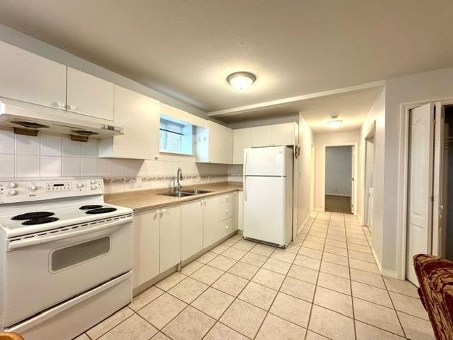 Kitchen with white appliances, white cabinets, decorative backsplash, light countertops, and under cabinet range hood | Image 4