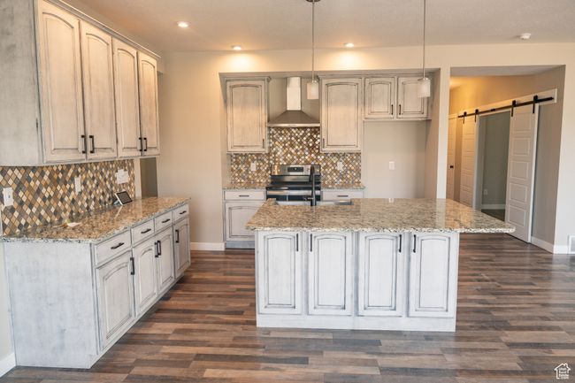 Kitchen with wall chimney range hood, electric stove, a barn door, a kitchen island with sink, and recessed lighting | Image 7
