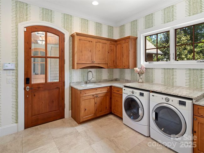 Enter the main level laundry/mudroom from the side breezeway, which adjoins the garage. The laundry room features Anna French wallpaper. Abundant room for laundry and storage as well as a window seat. Windows on both sides of the room allow for natural light all day long. Tile floor. | Image 34