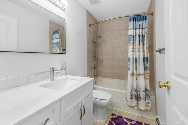 Full bathroom featuring shower / bathtub combination with curtain, vanity, tile patterned floors, toilet, and baseboard heating | Image 27