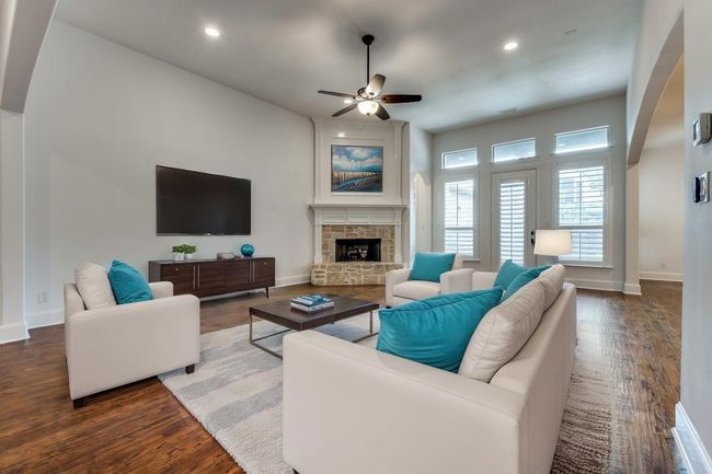 Living area with ceiling fan, arched walkways, wood finished floors, and a stone fireplace | Image 5