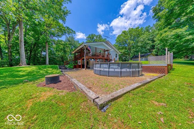 view of grassy yard with a deck, an outdoor pool, stairs, and view of wooded area | Image 65