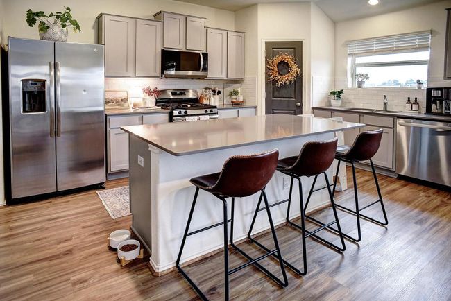 Kitchen featuring stainless steel appliances, a sink, a kitchen bar, decorative backsplash, and gray cabinetry | Image 11