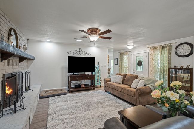 Living room with light wood-style floors, a ceiling fan, a fireplace, and crown molding | Image 5