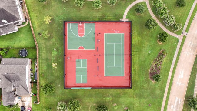 This aerial photo showcases a vibrant recreational area featuring a combined basketball and tennis court surrounded by lush green lawns. Nearby paths and landscaped areas enhance the community space, offering a great spot for outdoor activities within a residential neighborhood. | Image 46