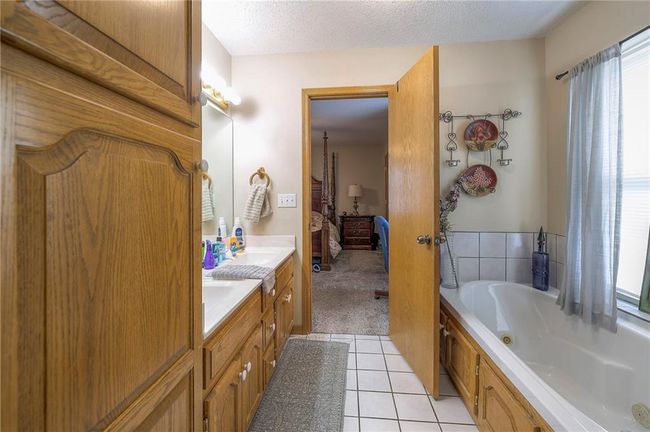 Ensuite bathroom featuring double vanity, a whirlpool tub, tile patterned flooring, and a textured ceiling | Image 20