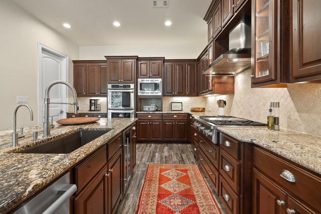 Kitchen featuring a sink, exhaust hood, appliances with stainless steel finishes, dark wood-style flooring, and light stone counters | Image 14