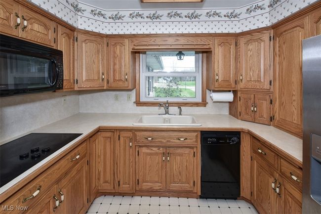 Kitchen with light countertops, brown cabinetry, a sink, and black appliances | Image 23