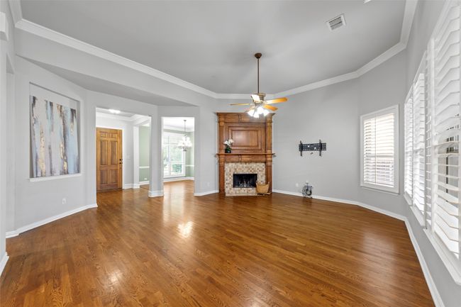 Unfurnished living room featuring a chandelier, a ceiling fan, a fireplace, dark wood-type flooring, and crown molding | Image 13