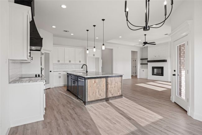 Kitchen featuring a sink, a fireplace, backsplash, an island with sink, and white cabinetry | Image 18