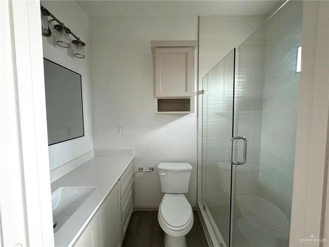 Bathroom with baseboards, toilet, a stall shower, wood finished floors, and vanity | Image 6