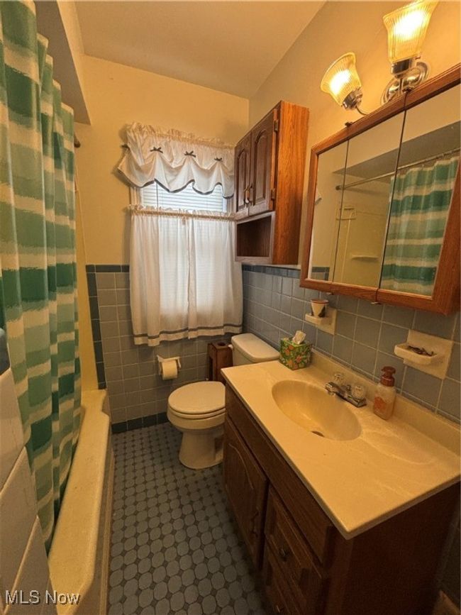 Bathroom with shower / tub combo, toilet, a wainscoted wall, vanity, and tile walls | Image 15